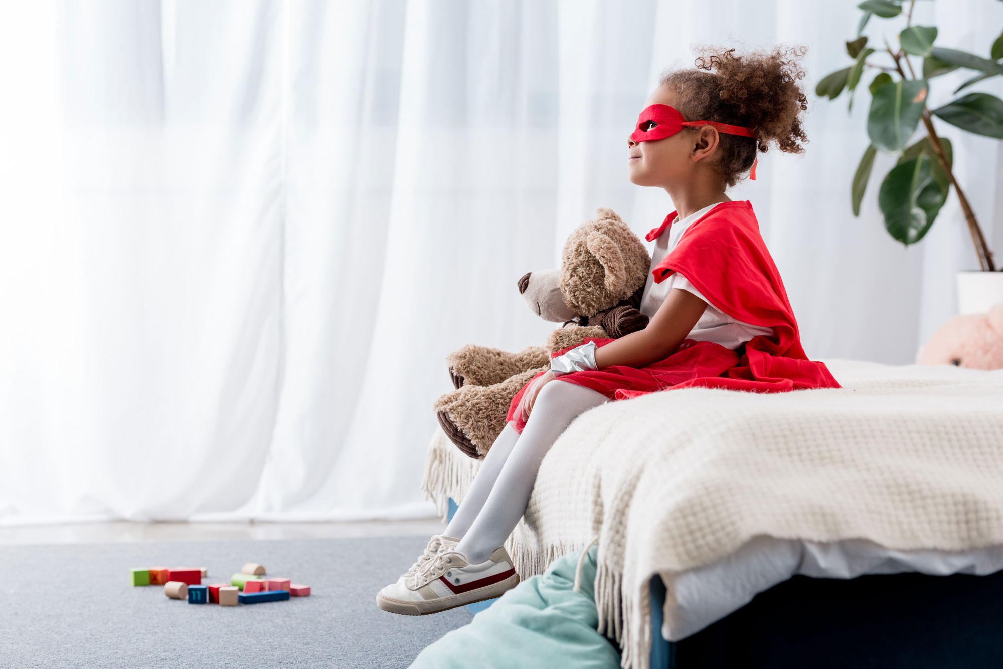 child sitting with a teddy bear and wearing a cape.